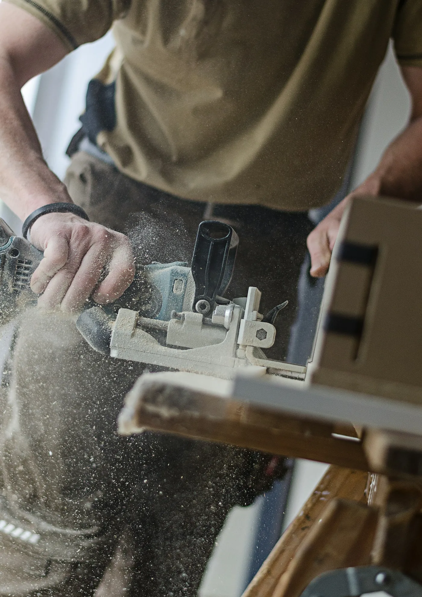 Carpenter using a joiner on a wooden board, with sawdust in the air